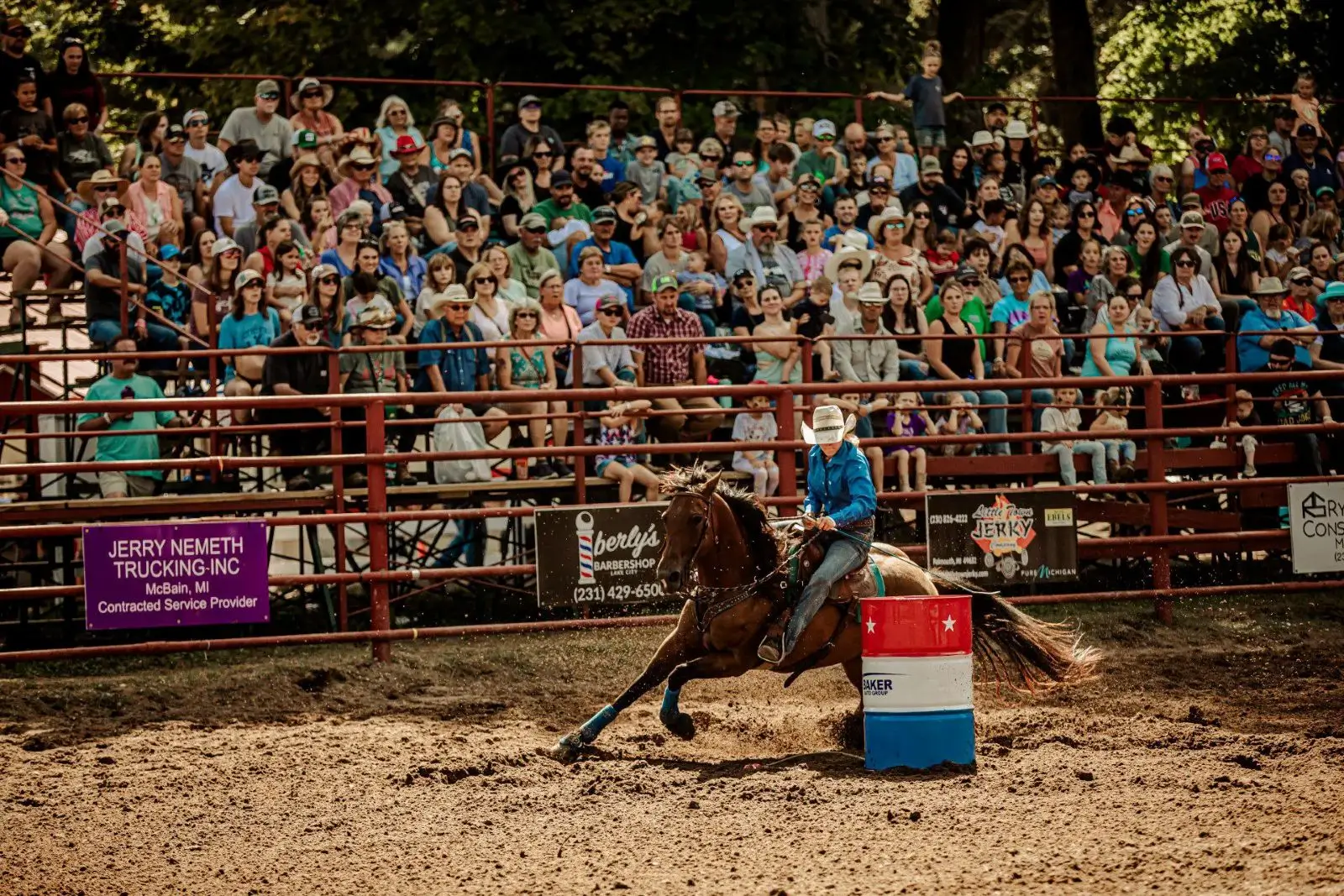 Cowboy racing a horse around a barrel in front of a crowd.