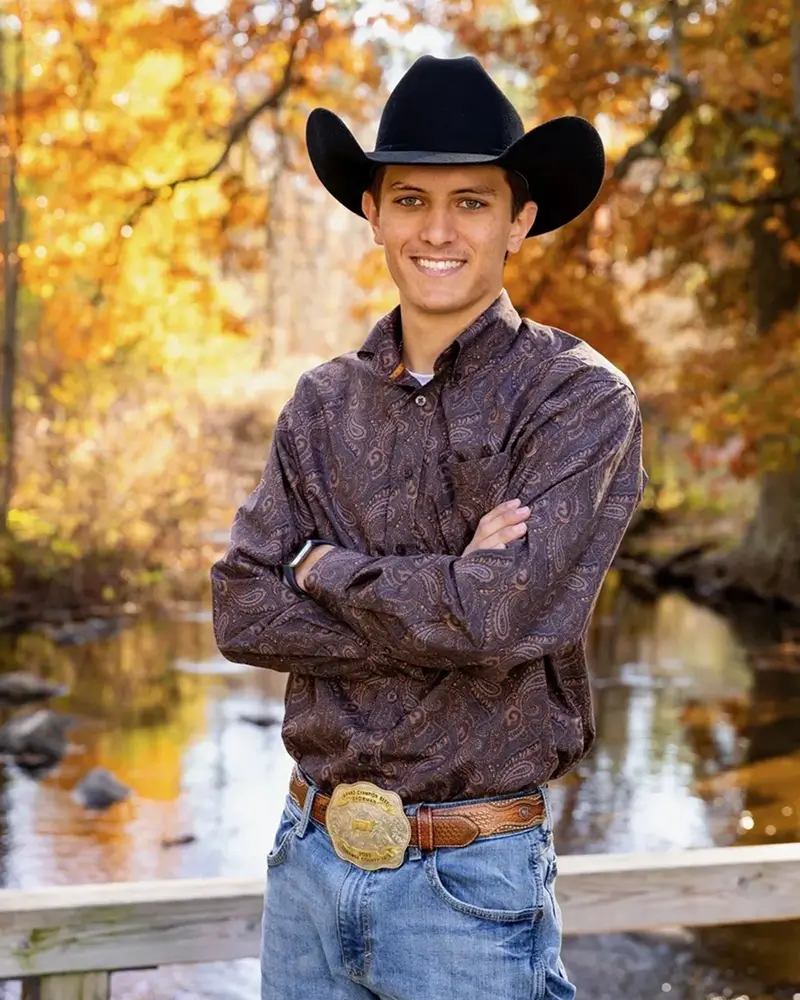 Young man in a cowboy hat standing by a creek in autumn.